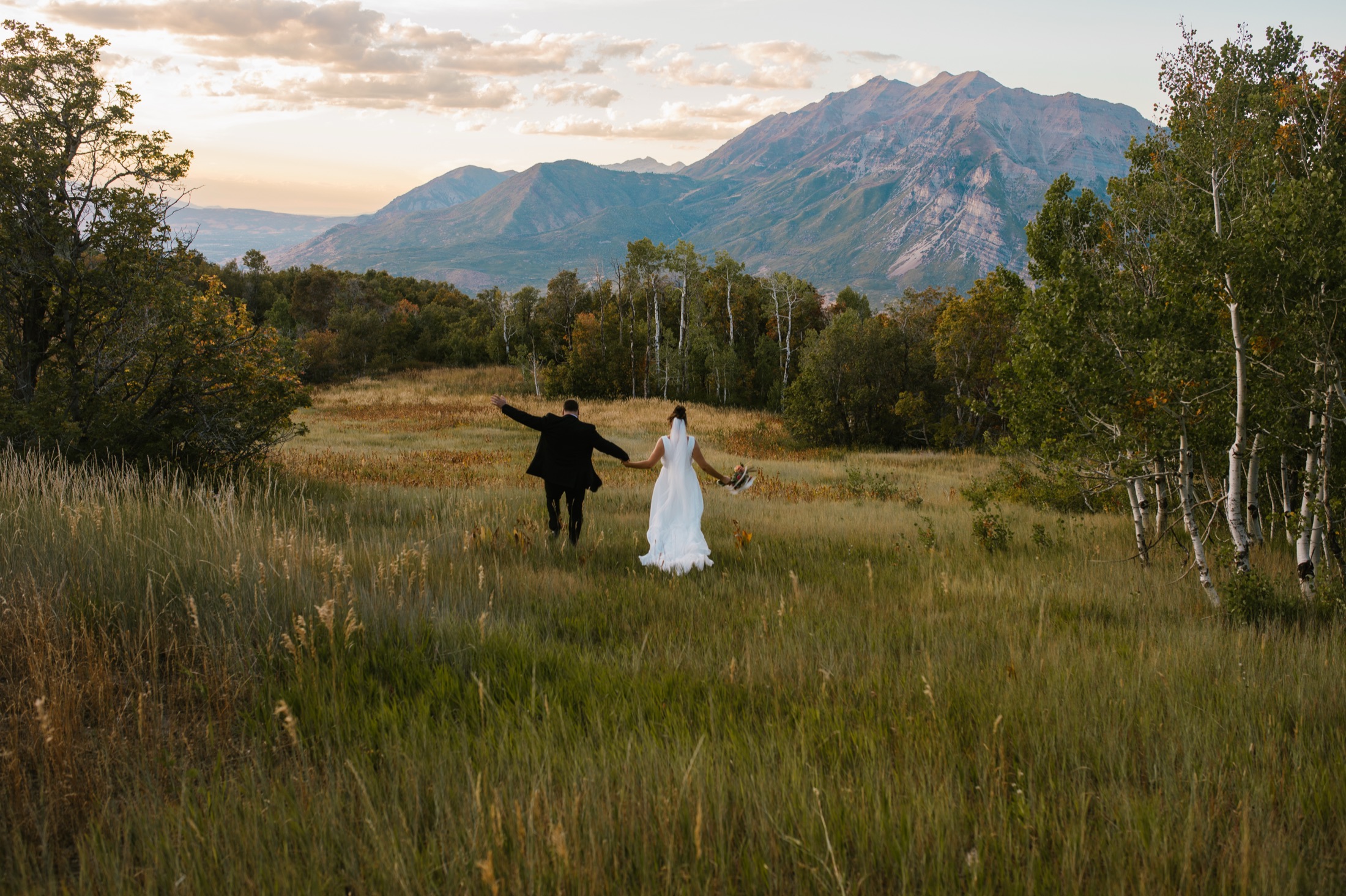 A couple running hand in hand through a mountain meadow in Utah at the end of summer.