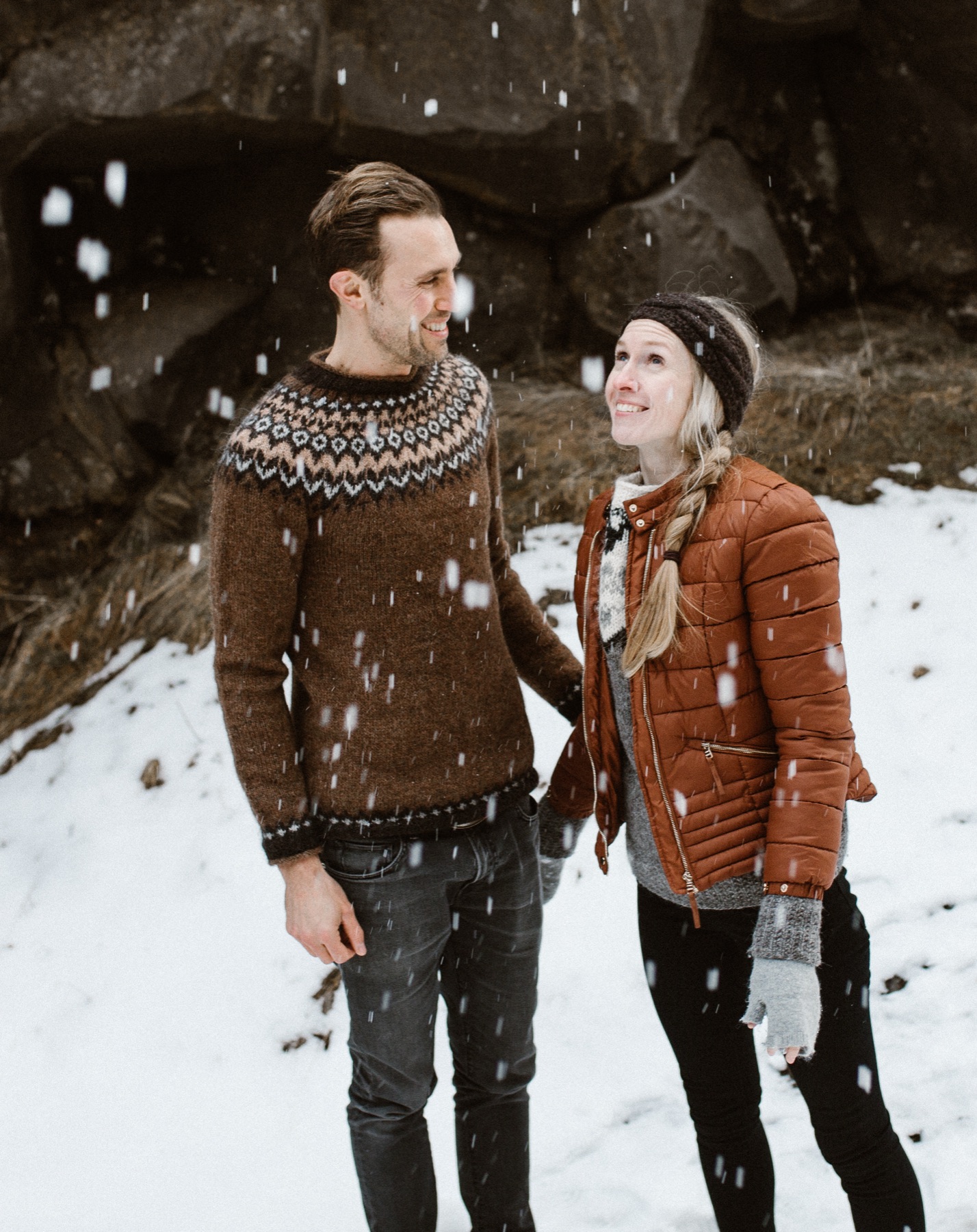 A couple in wool sweaters laughing in falling snow in Iceland.
